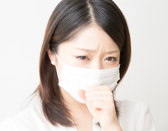 マスクをして咳込んでいるいる女性の写真